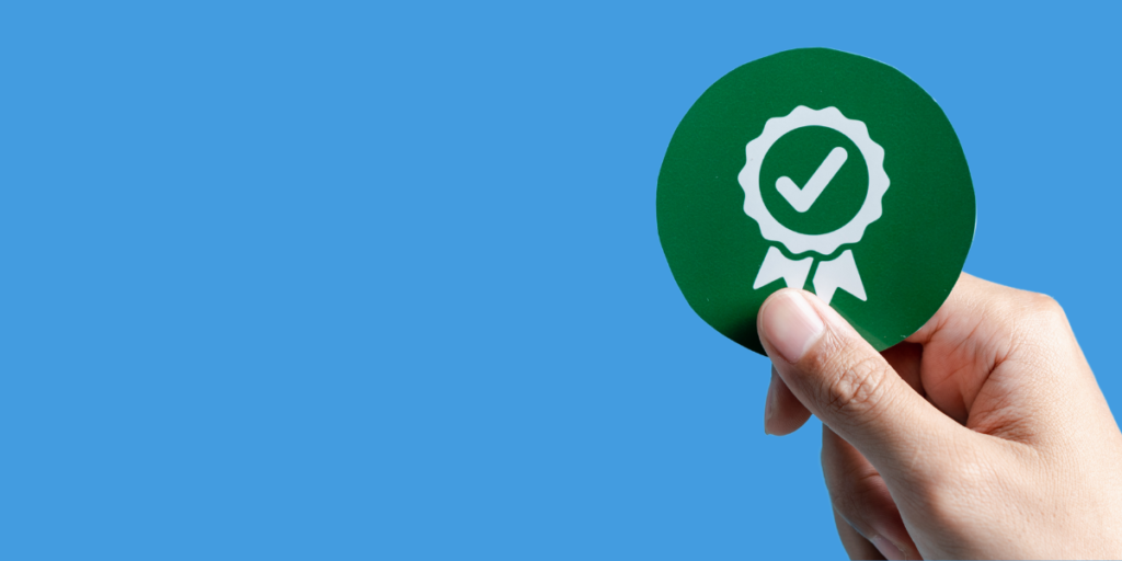 Mão segurando selo verde de certificação, simbolizando qualidade em automação industrial e sistemas de controle.