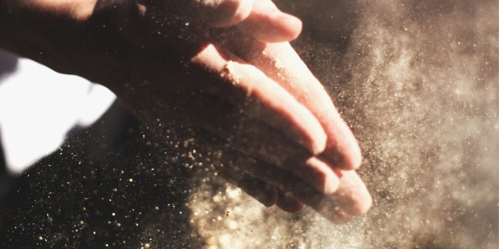 Mãos limpando pó, representando a importância do despoeiramento em processos industriais e automação.